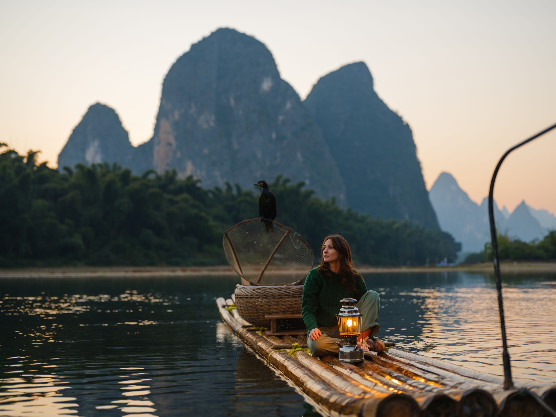 Woman with lantern on wooden raft in Xingping, Guilin, China at sunset